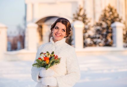 gelukkige en mooie vrouw met Royalwaardige Oorbellen in glimlacht en houdt boeket van oranje rozen vast, winterse achtergrond